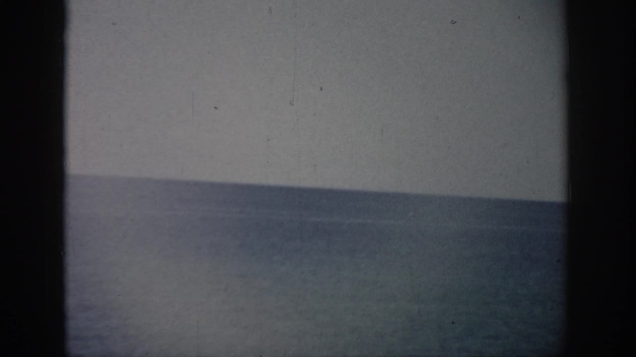 1959 Florida 8mm frame showing a muted ocean horizon under pale sky with grain, dust, and dark rounded film edges.