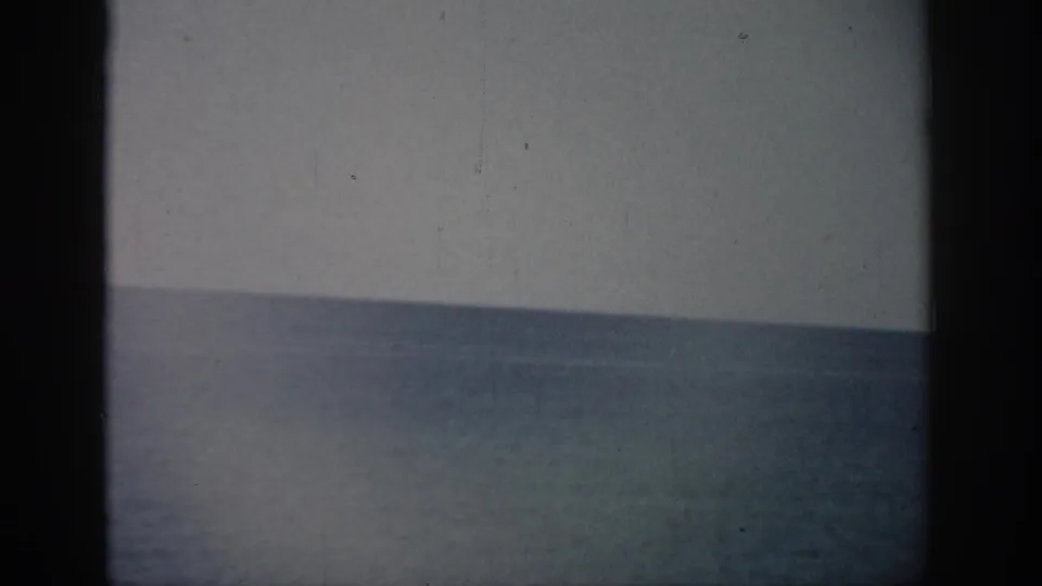1959 Florida 8mm frame showing a muted ocean horizon under pale sky with grain, dust, and dark rounded film edges.