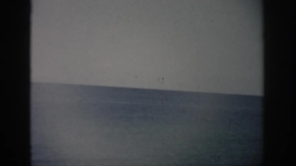 1959 Florida home-movie frame with the sea meeting a pale sky, softened by grain, fading, and dark 8mm frame edges.