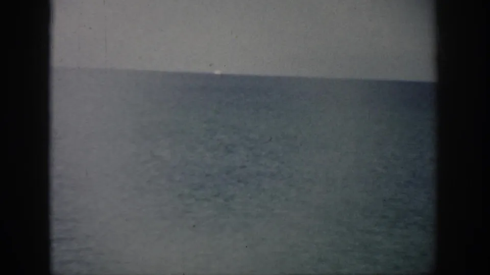 1959 Florida coastal frame showing calm ocean water below a pale sky, with soft exposure and visible 8mm film wear.