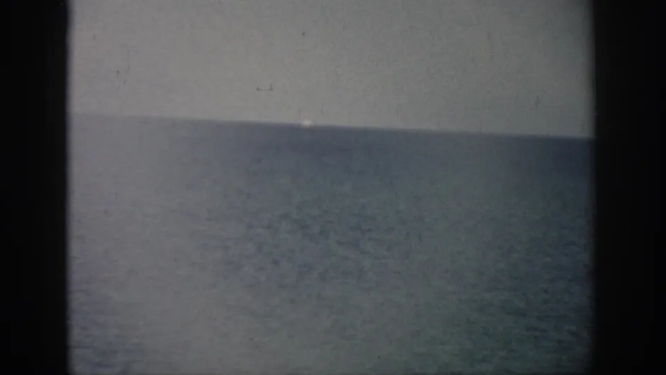 1959 Florida 8mm frame showing a still ocean horizon, pale sky, soft contrast, grain, and dark film borders.
