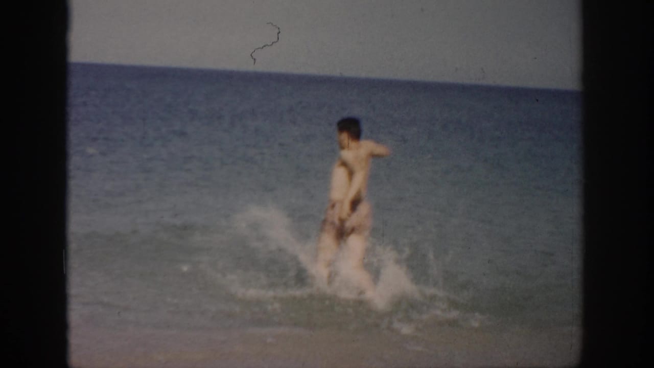 Man in swim trunks splashing through shallow ocean water near the beach.