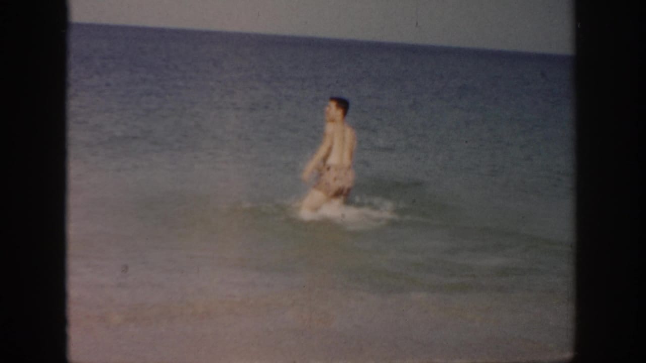 Man wading forward in calm ocean water with small waves around his legs.