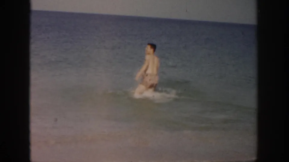 1959 Florida beach footage shows the man wading into calm blue-green ocean water under a simple horizon.