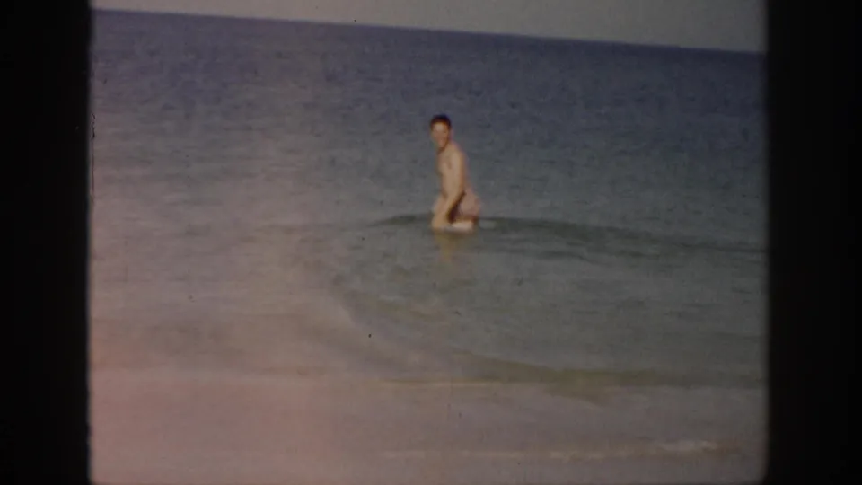 Final 1959 Florida home-movie frame shows the man partly submerged in shallow ocean water with a small wave in front of him.