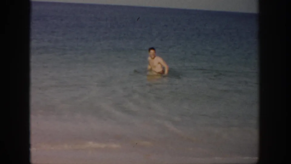 1959 Florida beach footage frame with a man standing farther out in the ocean, filmed from shore.