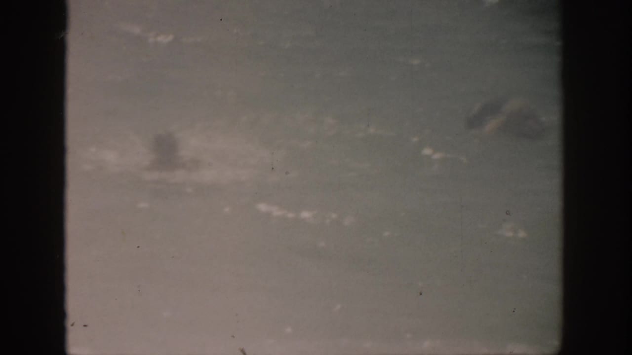 Distant swimmer in open ocean with a hazy horizon and dark film borders.