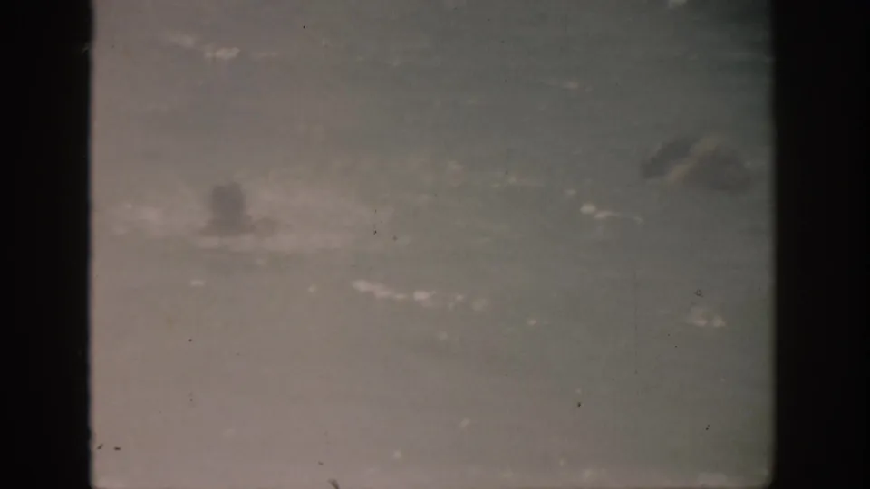 1959 Florida 8mm frame showing a distant swimmer silhouette in the ocean beneath a soft, hazy horizon.