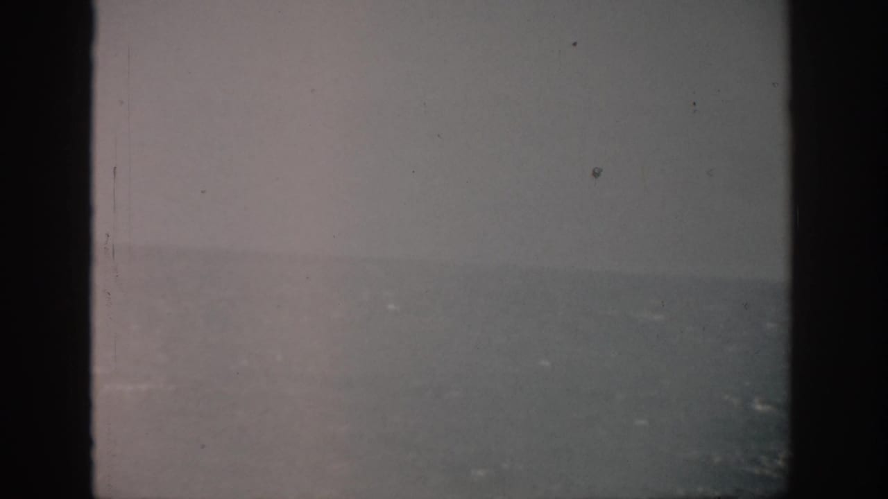 1959 Florida 8mm frame showing a soft gray sea horizon beneath gloomy sky, bordered by dark film edges and visible dust.