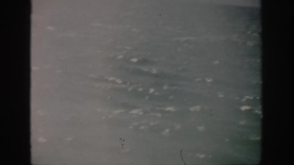 1959 Florida 8mm frame showing calm open ocean under hazy overcast light, with dark gate edges and surface whitecaps.