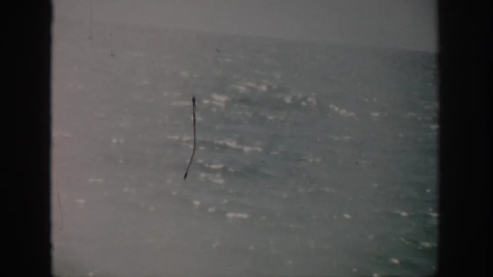 1959 Florida 8mm view of bright blue water sparkling beyond a dark window edge, with film scratches and soft exposure.