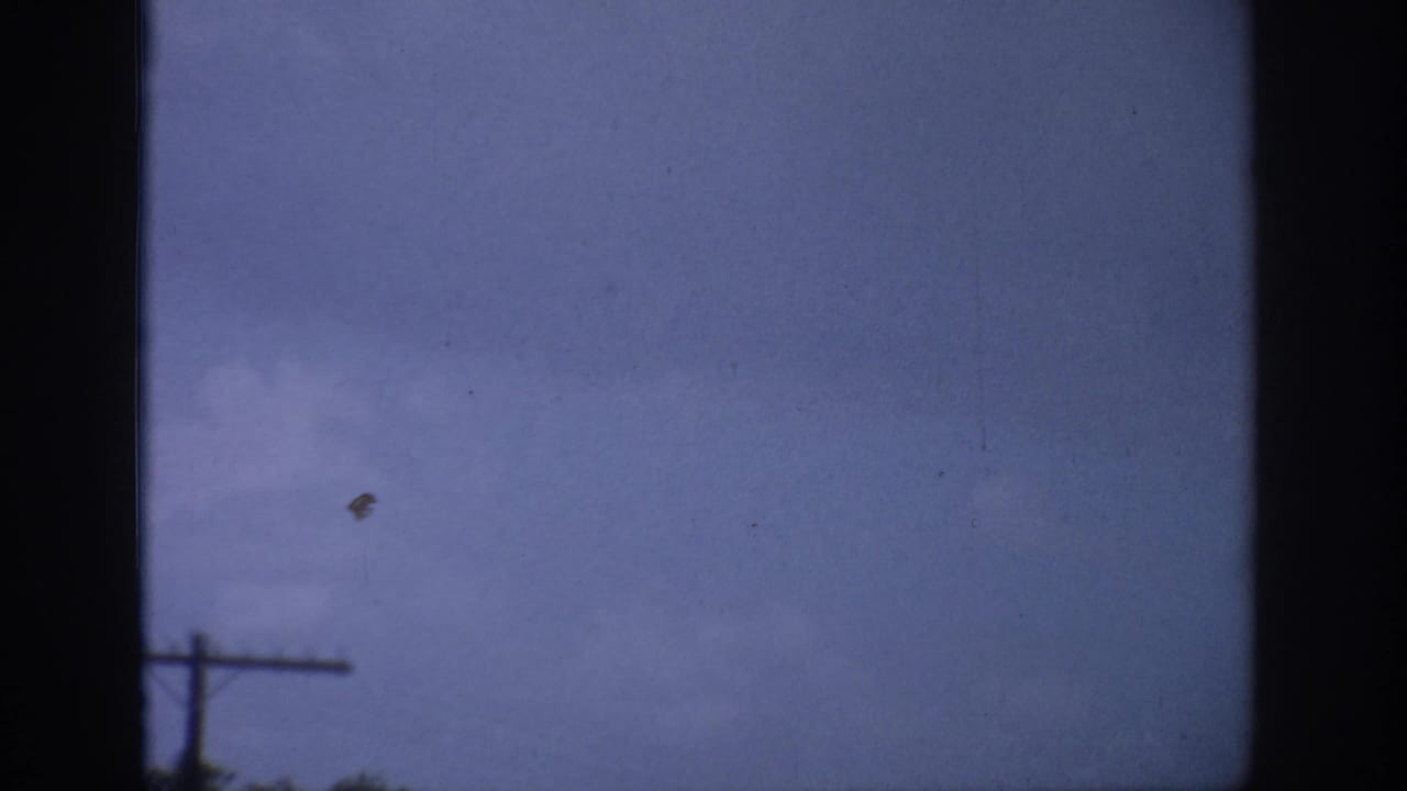 Dark window frame around cloudy sky with a small dark object and a telephone pole near the horizon.