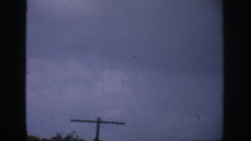 1959 Florida home-movie frame with a dark vertical window division, muted sky, and telephone pole at the lower edge.