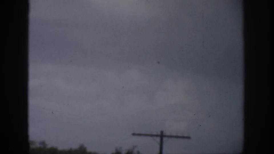 Faded 1959 Florida 8mm view of overcast sky, dark frame edges, a low tree line, and a telephone pole.