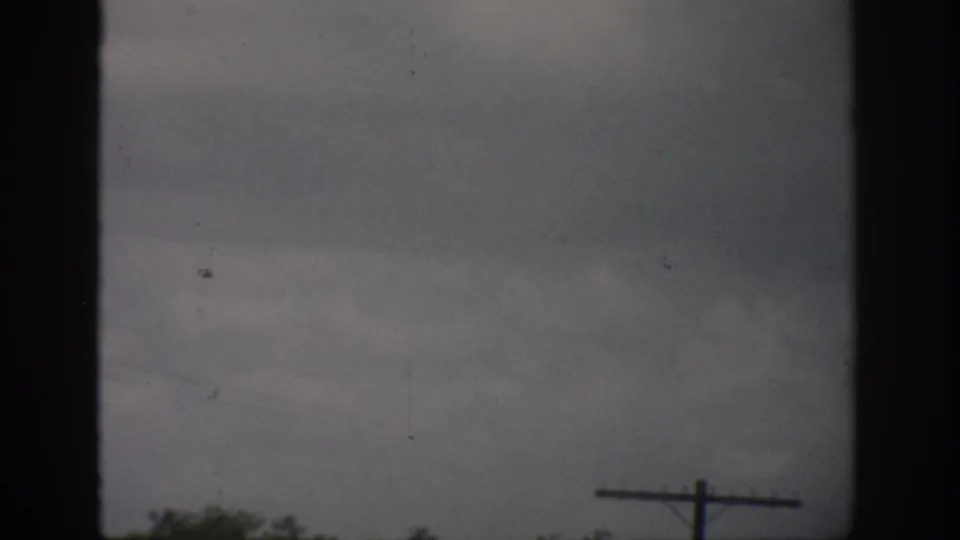 1959 Florida 8mm frame showing pale cloudy sky, dark window borders, low trees, and a telephone pole at lower right.