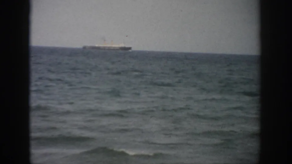 1959 Florida 8mm frame showing a distant ship offshore, low waves, and a pale overcast sky.