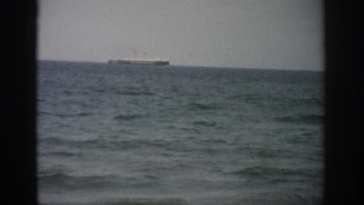 Distant ship on the horizon beyond a dark window frame and choppy sea.