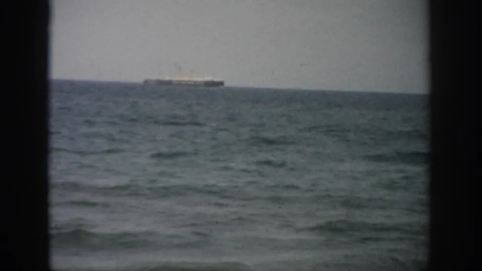 1959 Florida 8mm frame showing a distant ship on the ocean horizon, seen through dark vertical framing under an overcast sky.