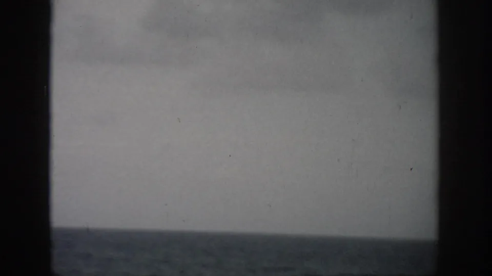 1959 Florida home-movie frame with open sea, low horizon, and cloudy sky seen through dark vertical frame bars.
