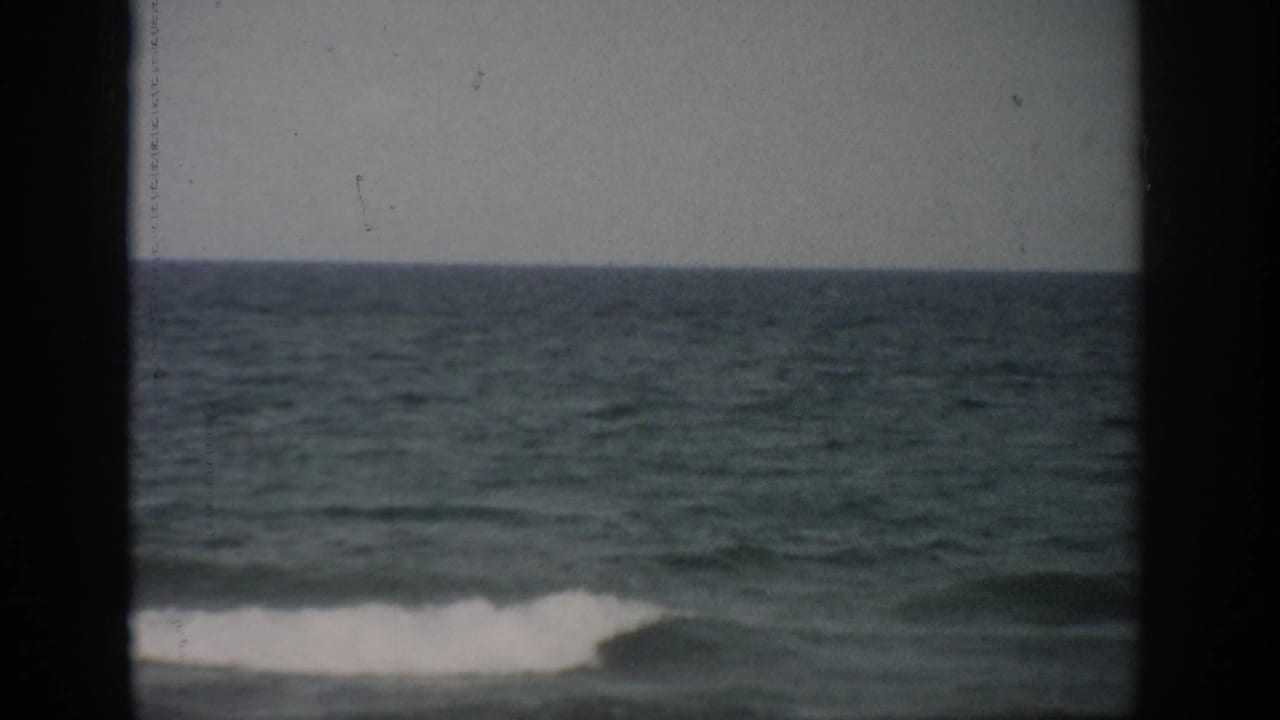 1959 Florida coastal footage shows a small white wave breaking across green-blue water, partly divided by a dark frame edge.