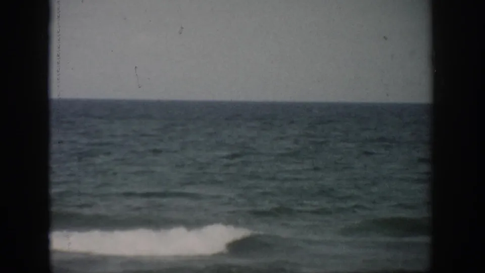 1959 Florida coastal footage shows a small white wave breaking across green-blue water, partly divided by a dark frame edge.