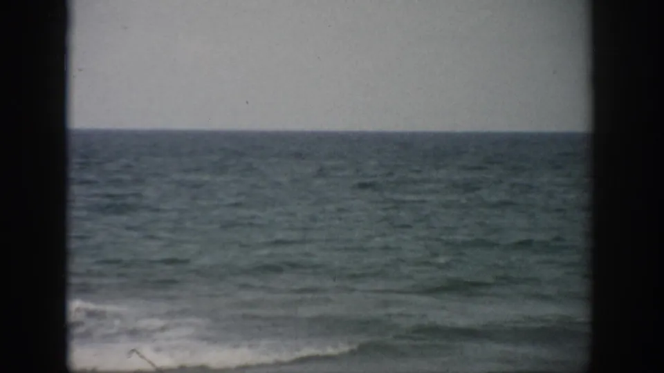 1959 Florida 8mm frame with a gray sky, steady ocean horizon, and gentle white surf along the lower edge.