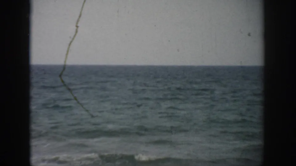 1959 Florida coastal view with muted blue-gray sea, dark framing, and visible 8mm film wear.