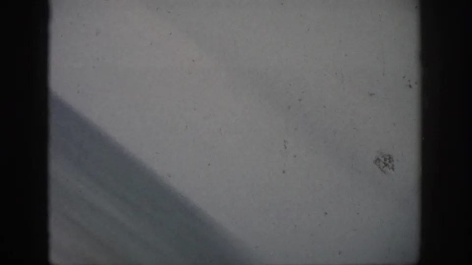 Soft, underexposed 1959 Florida 8mm frame with window edge, pale foreground, and partial sea view.