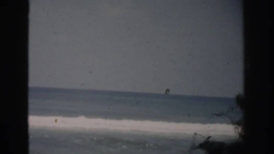 1959 Florida 8mm coastal frame showing surf, horizon, dark window edge, and a small bird-like speck near the sky.