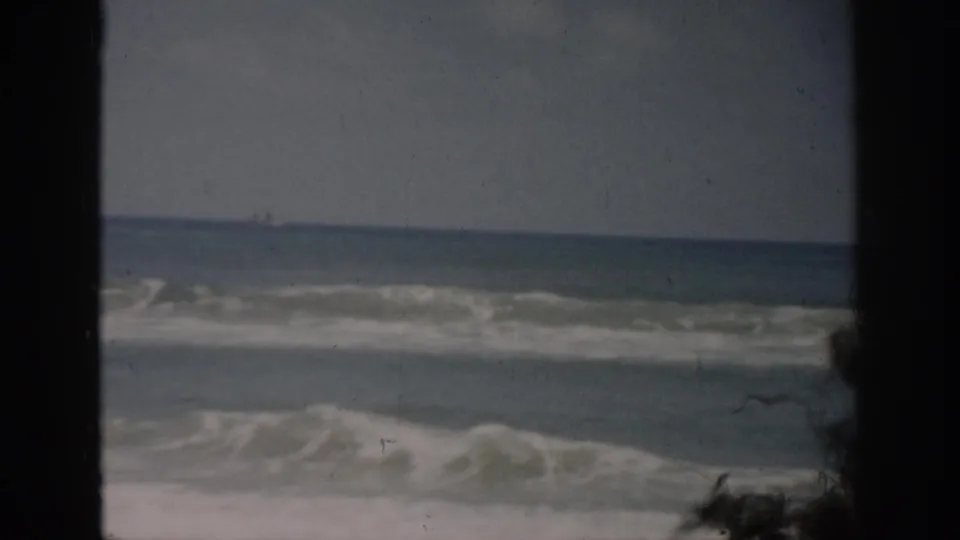 1959 Florida 8mm frame showing ocean surf and a faint distant ship on the horizon, bordered by dark window-like edges.