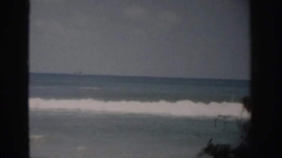 1959 Florida home-movie frame showing a white band of breaking surf, open water, and dark vertical borders around the coastal view.