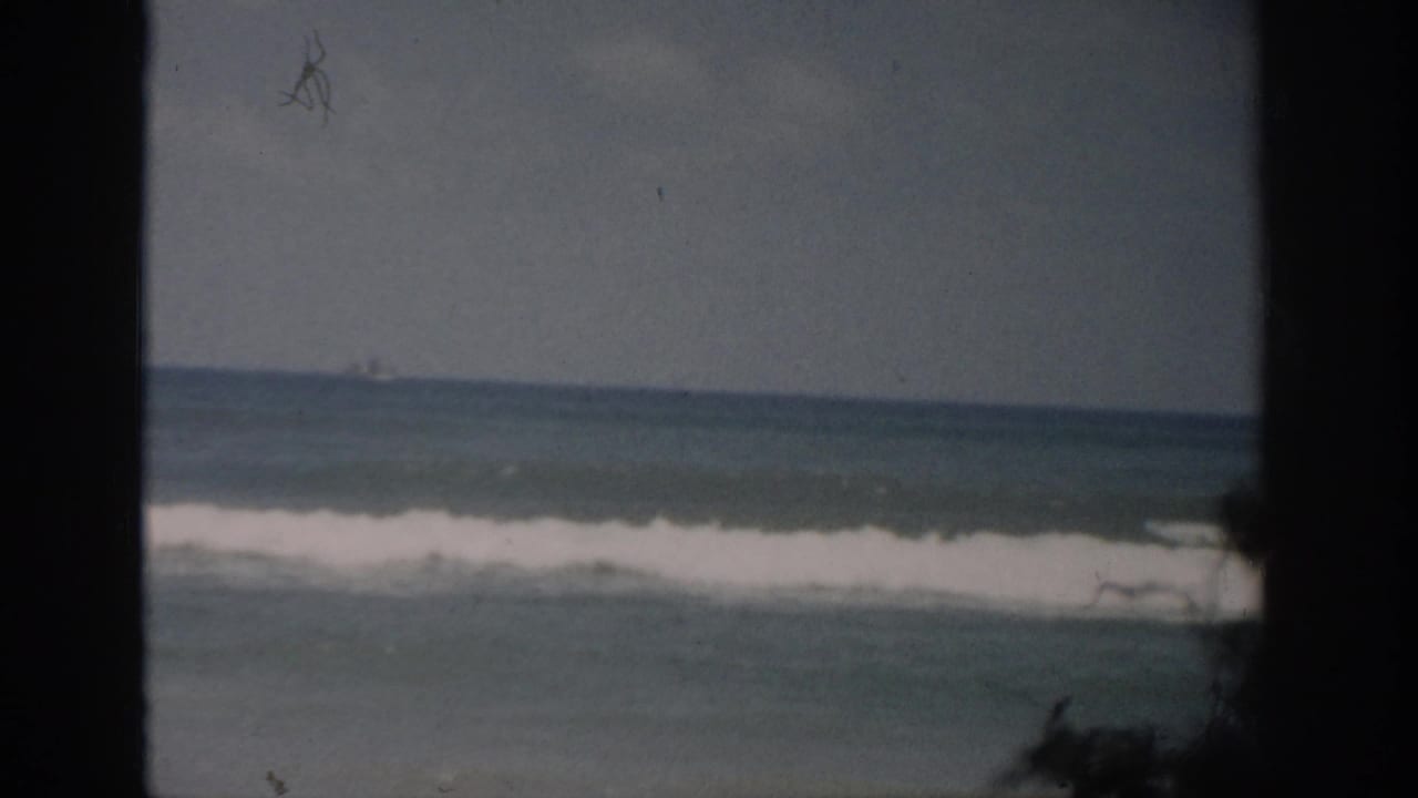 Ocean waves and white surf seen through dark vertical window framing.