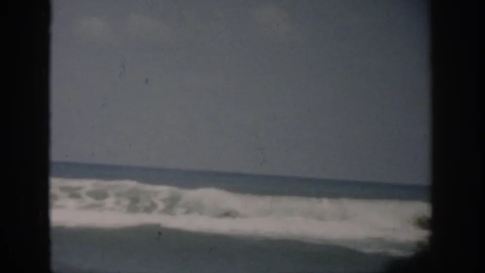 1959 Florida home-movie frame showing a breaking wave and foamy surf viewed through dark foreground framing.