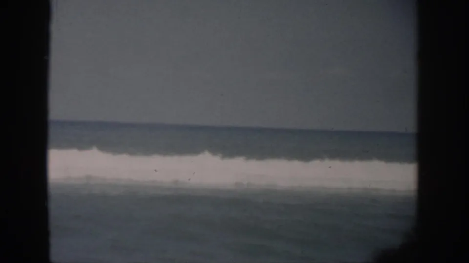 1959 Florida coastal home-movie frame of rolling surf and white foam, bordered by dark window framing.