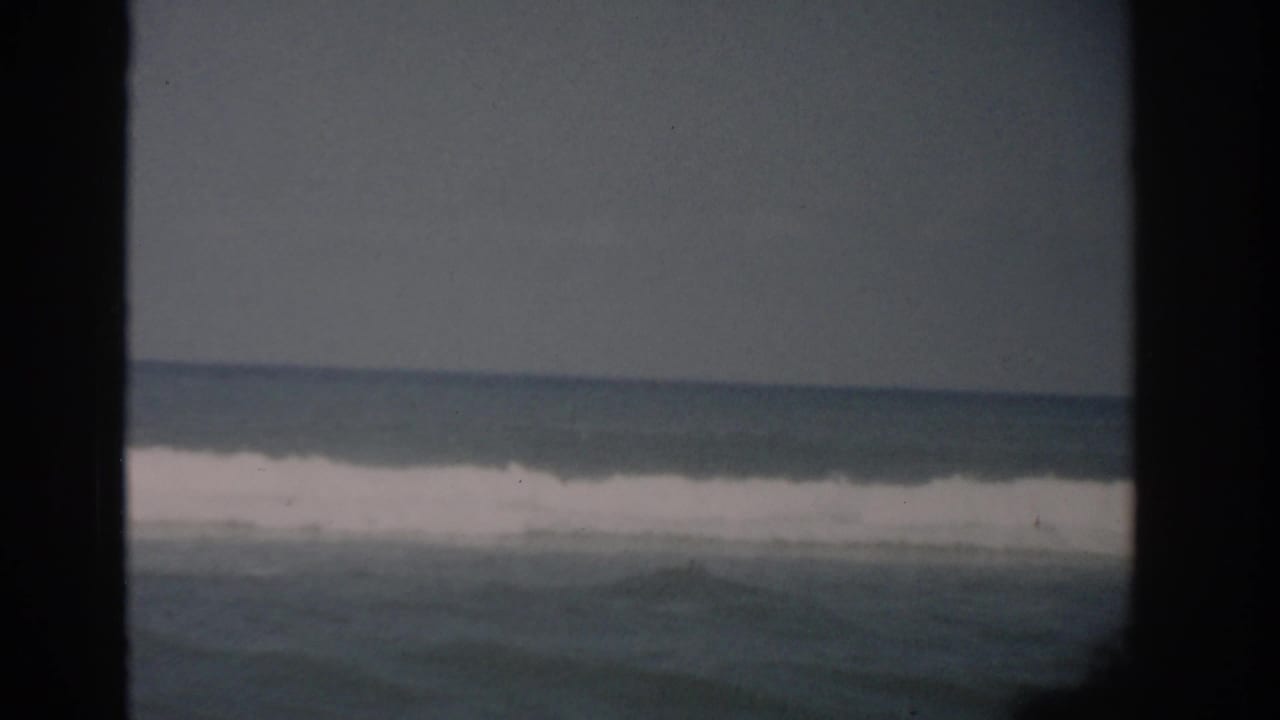 Ocean waves seen through a dark window frame under a hazy sky.