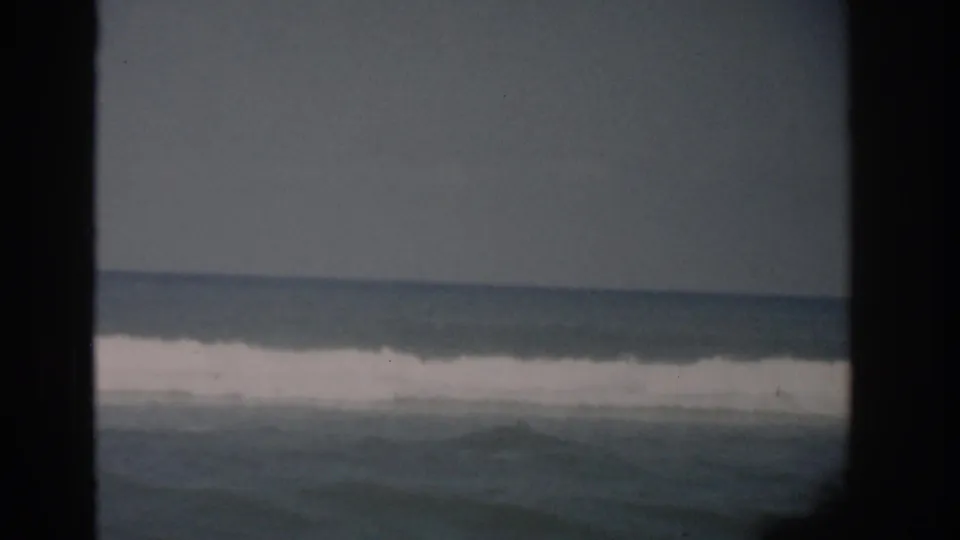 1959 Florida home-movie frame showing blue-gray ocean surf viewed through a dark window mullion, with a faint horizon line.