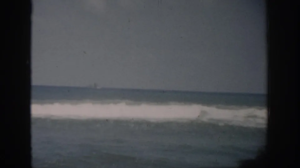1959 Florida home-movie view of calm surf and horizon through a dark window frame, with muted color and visible grain.