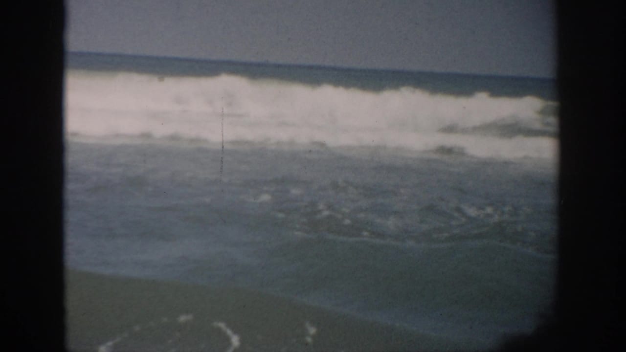 1959 Florida coastal frame with white surf breaking across choppy ocean water beneath a clear, muted sky.