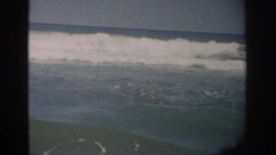 1959 Florida coastal frame with white surf breaking across choppy ocean water beneath a clear, muted sky.