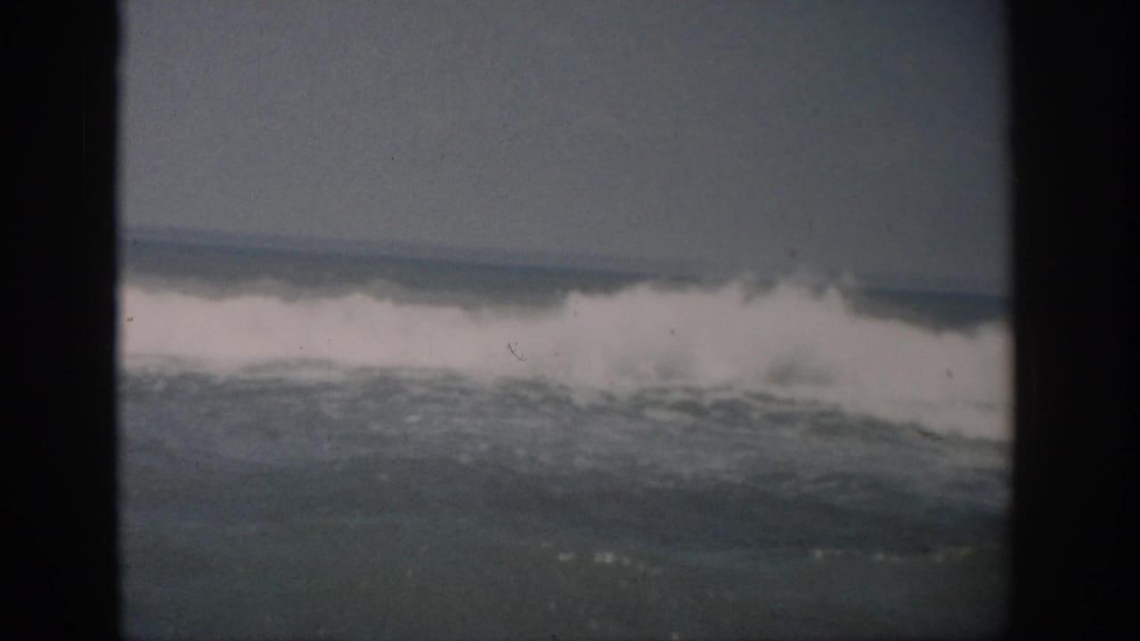 A breaking ocean wave crests across the frame with dark vertical film borders at the sides.