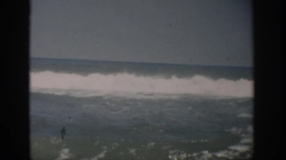 1959 Florida 8mm frame showing a foamy wave line and choppy water near the beach, with muted color and visible film specks.
