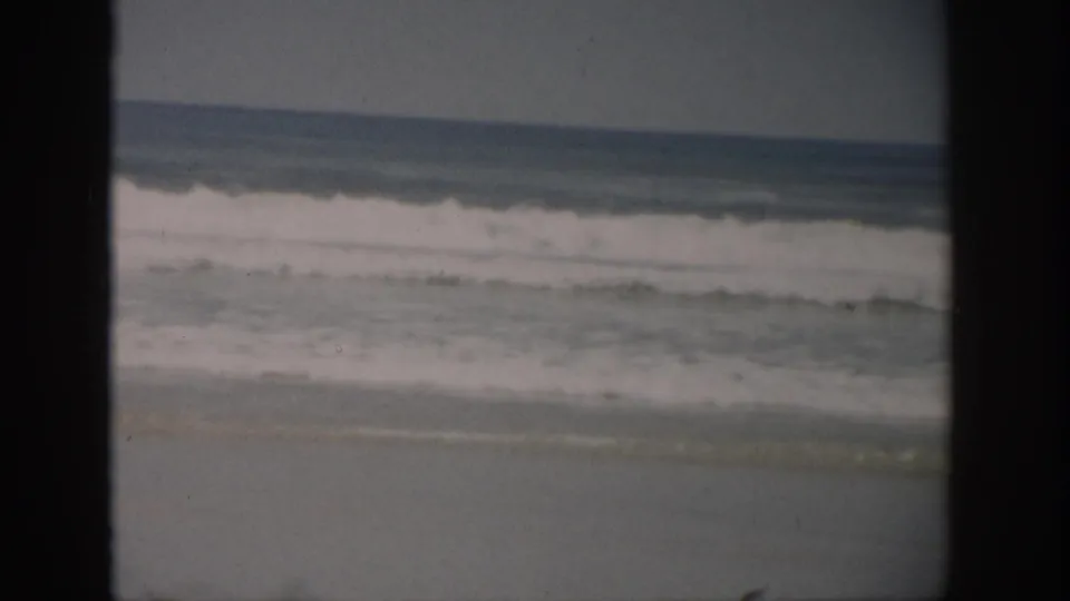 1959 Florida shoreline view with white-capped surf, wet sand, muted sky, and visible 8mm frame borders.