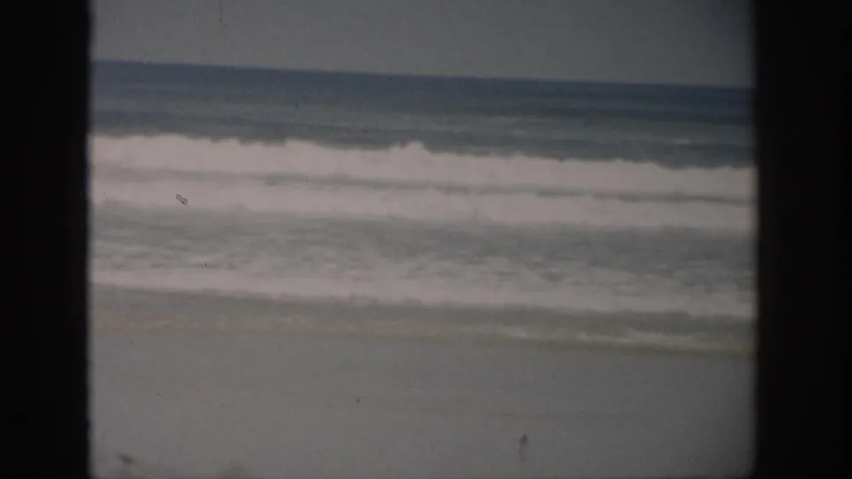 Faded 1959 Florida beach footage shows layered surf moving toward shore, with visible grain and frame-edge darkness.