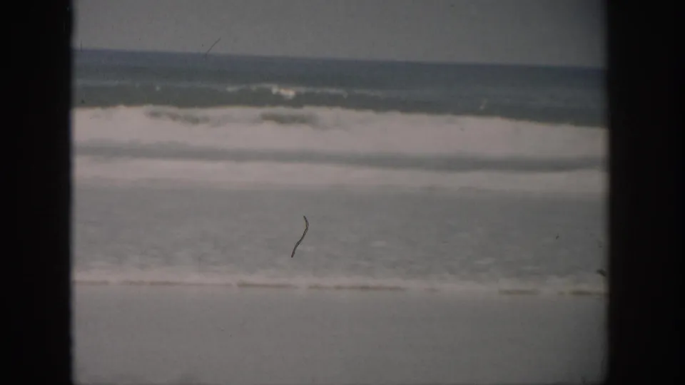 1959 Florida home-movie still of waves breaking near shore, with soft exposure, grain, and small visible film marks.