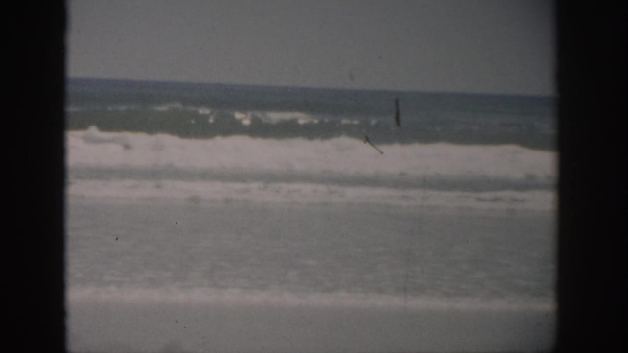Ocean waves breaking toward a beach, framed by dark 8mm film borders.