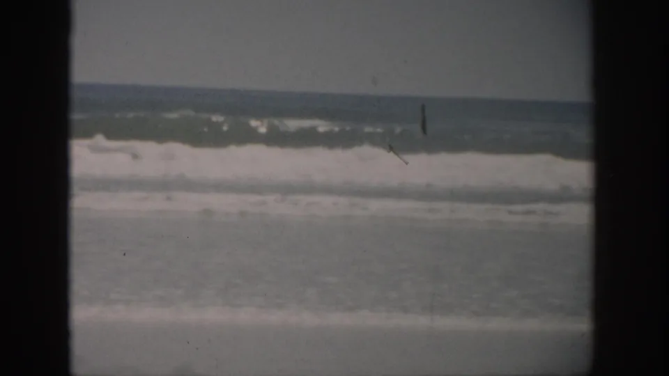 1959 Florida 8mm home-movie frame of rolling ocean surf under a muted sky, with dark gate borders and visible film grain.