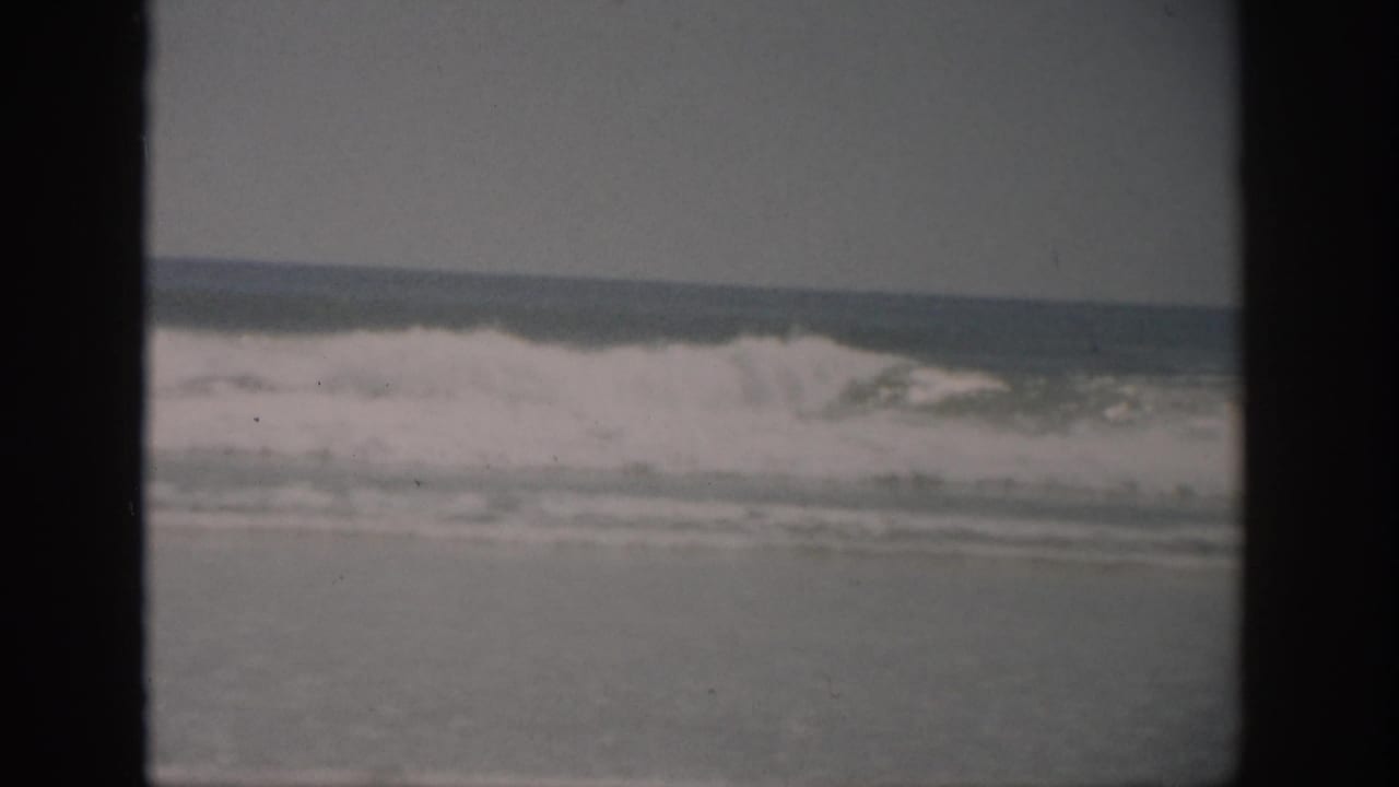 White surf rolls across the ocean with a dark vertical film border at left.