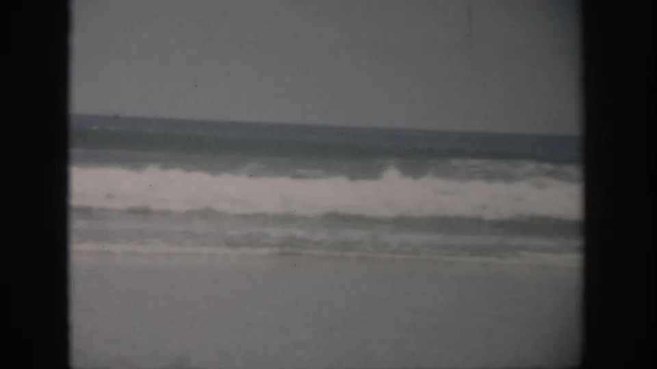 1959 Florida home-movie frame showing ocean waves and a distant horizon, with aged 8mm grain and dark gate borders.