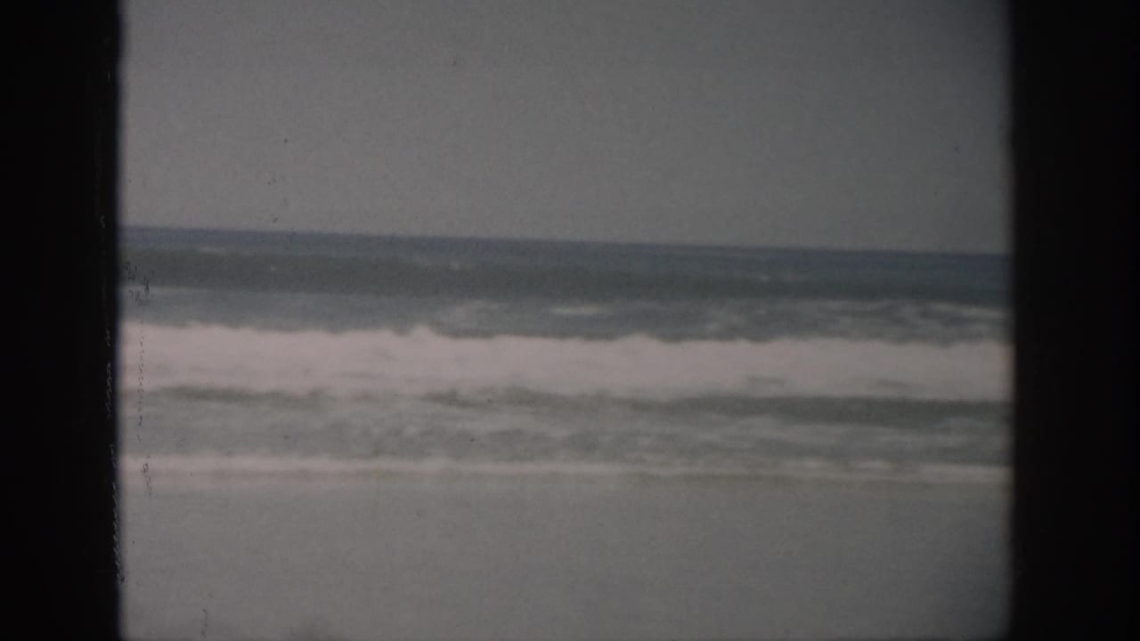 1959 Florida 8mm frame showing surf breaking onto a sandy shoreline under an overcast sky, with dark reel borders visible.