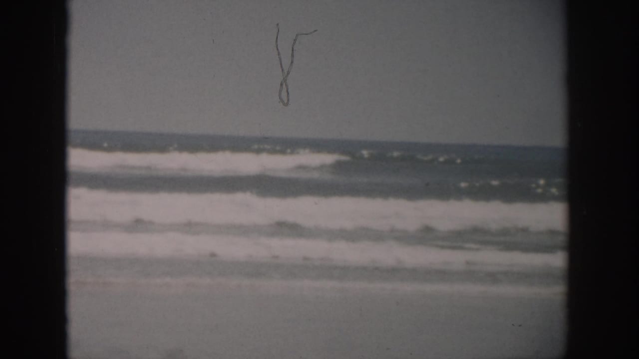 1959 Florida 8mm frame showing white surf rolling toward wet sand under an overcast horizon.
